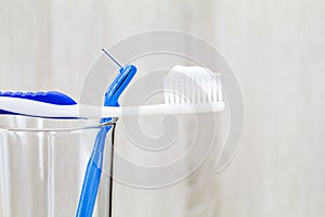 Toothpaste on toothbrush and interdental brush on clean glass on blurred wooden background in bathroom