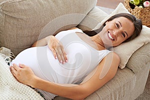 Toothy smiling woman embracing belly on sofa