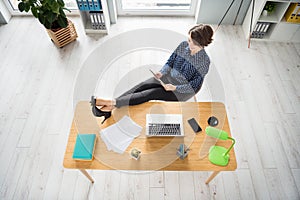 Top above high angle view of nice cheerful focused girl sitting in chair putting legs on table using ebook at workplace