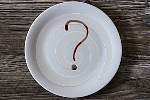 Top above overhead close up view photo of white plate crockery on wooden table. A plate with question mark on it, written with cho
