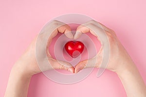Top above overhead pov first person  view close up photo of heart-shaped hands and a red heart  isolated on pastel pink color
