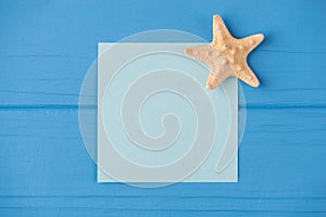 Top above overhead view close-up photo of a blank note with a small starfish isolated on blue wooden background with copyspace