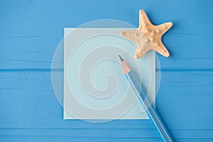 Top above overhead view close-up photo of a blank note with a small starfish and a pencil isolated on blue wooden background with