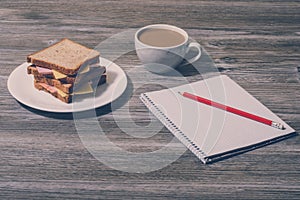 Top above overhead view phot of break rest relax snack at work. Cheese sandwich with cup of white coffee, notebook and pencil. Hor