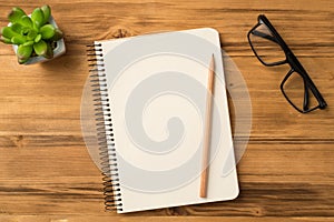 Top above overhead view photo of empty blank notepad on spiral with clear page pencil eyeglasses on table and plant laying om