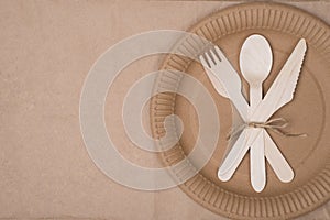 Top above overhead view photo of a set of wooden cutlery lying on a paper plate placed to the right side isolated on craft paper photo