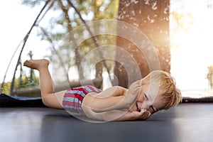 Top above view of cute little caucasian funny blond toddler boy lying inside big black trampoline at home backyard