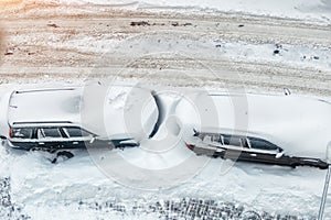 Top aerial view of apartment office building parking lot with many cars covered by snow stucked after heavy blizzard snowfall