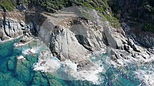 Top aerial view of azure ocean and huge waves crashing on rocky cliffs with splashing water and white foam, Cap Corse, Corsica