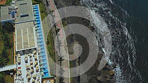 Top aerial view : flying over island seashore with palms, waves and people walking near water.