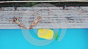 Top aerial view of two women lying at the pool with inflatable mattress in a pineapple shape. On holidays having fun and