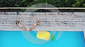 Top aerial view of two women lying at the pool with inflatable mattress in a pineapple shape. On holidays having fun and