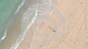 Top aerial view of woman relaxing on sand beach and ocean turquoise foam waves rolling at tropical beach. Drone goes up