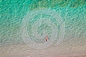 Top, aerial view. Young beautiful woman in a red bikini panties swimming in sea water on the sand beach. Drone, copter photo.