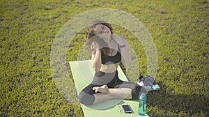 Top angle view of cheerful Caucasian sportswoman sitting on exercise mat and warming up. Portrait of young slim woman