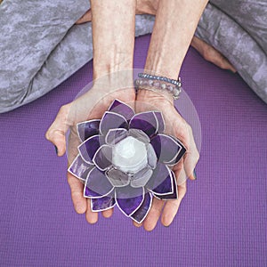 Top angle view of hands holding a purple glass lotus. Yoga and meditation concept