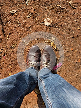 Top angle view of men leg in Blue color jeans with old damaged brown color shoes on stony clay ground on background. Picture