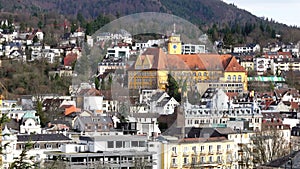 Top bird eye view of Baden-Baden city with buildings with tiled roofs between mountains in spring sunny day. Baden