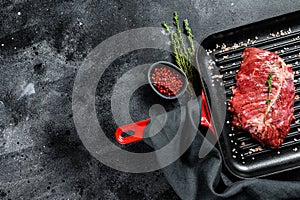 Top blade steak on a grill pan, raw meat, marbled beef . Black background. Top view. Copy space