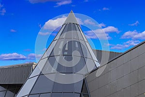 The top of the building is glass against the background of clouds and blue sky.