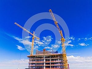 Top of a building with yellow cranes on a blue sky