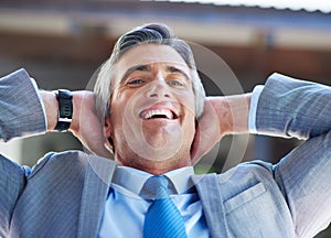 On top of the business world. a content businessman leaning back in his chair with his hands behind his head.