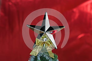 Top of Christmas tree decorated with star in bright red shiny background