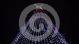 The top of a Christmas tree with a star and colorful lights and decorations against the background of the night sky