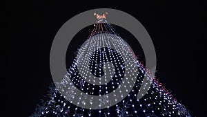 The top of a Christmas tree with a star and colorful lights and decorations against the background of the night sky