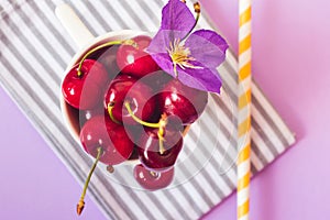 Top view of cherries on a stripped cloth and a yellow stripped straw on purple background