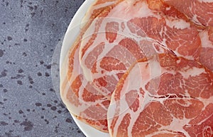 Top close view of a plate of dry coppa on a gray mottled tabletop