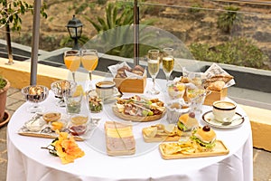 Top closeup of a round table outdoors with white tablecloth and burgers, chips, glasses of champagne