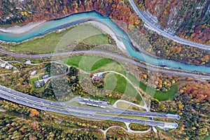 Top dawn aerial view of freeway speed road going out from undeground tunnel between yellow autumn forest trees and blue river