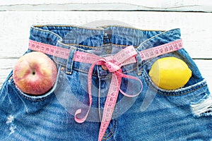 Top of denim trousers with Apple and lemon, on a wooden background. Blue jeans with a measuring tape instead of a belt. jeans with