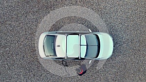 Top down aerial drone shot as man attaches loading straps to roof rack bars on a silver car