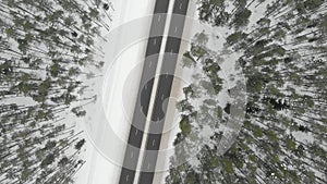 Top down aerial spinning view of snow covered forest with a two-lane road