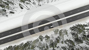 Top down aerial spinning view of snow covered forest with a two-lane road