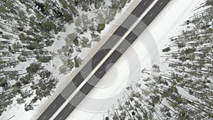 Top down aerial spinning view of snow covered forest with a two-lane road