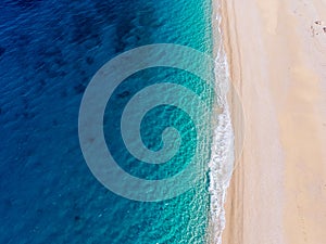 Top-down aerial view of a white sandy beach on the shores of a beautiful turquoise sea.