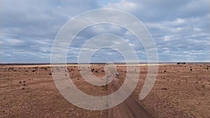 Top down aerial view of fast driving car or jeep on dirt road leaving cloud of dust behind. blue sky with clouds