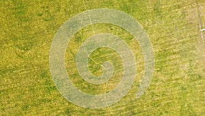 Top down aerial view of football field surface covered with green grass and sprinklers spraying water.