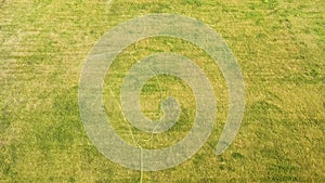 Top down aerial view of football field surface covered with green grass and sprinklers spraying water.