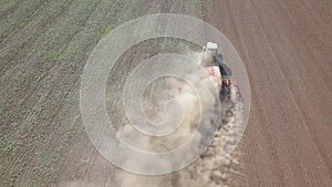 Top down aerial view of green tractor cultivating ground and seeding a dry field. Farmer preparing land with seedbed cultivator as