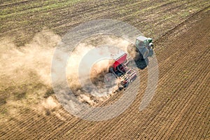 Top down aerial view of green tractor cultivating ground and seeding a dry field. Farmer preparing land with seedbed cultivator as