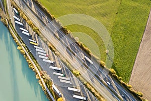 Top down aerial view of highway interstate road with fast moving traffic and parking lot with parked lorry trucks