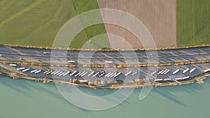 Top down aerial view of highway interstate road with fast moving traffic and parking lot with parked lorry trucks.