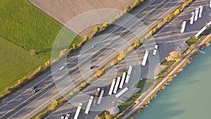 Top down aerial view of highway interstate road with fast moving traffic and parking lot with parked lorry trucks.