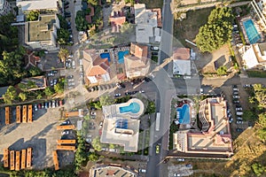 Top down aerial view of hotels roofs, streets with parked cars and swimming pools with blue water in resort city near the sea