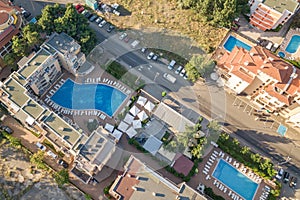 Top down aerial view of hotels roofs, streets with parked cars and swimming pools with blue water in resort city near the sea