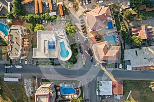 Top down aerial view of hotels roofs, streets with parked cars and swimming pools with blue water in resort city near the sea